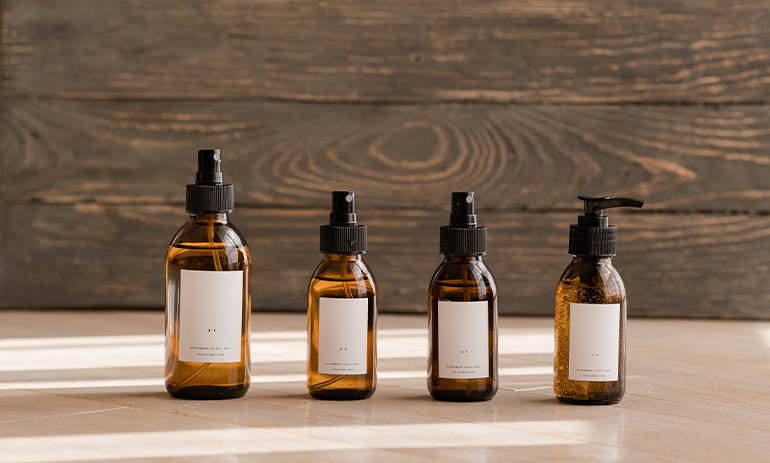 A line of beauty products in brown bottles sit on a wooden bench top