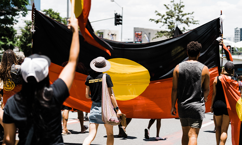 People marching carrying Aboriginal flag at Invasion Day rally Brisbane 2021.