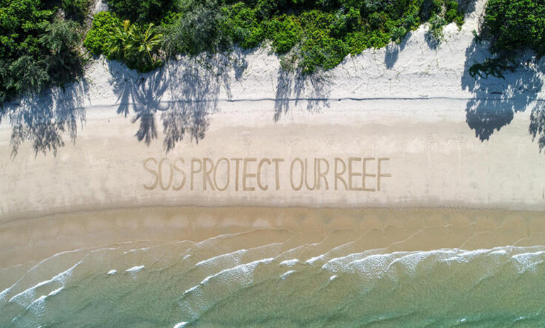 aerial view of words "SOS protect our reef" written in the sand on a beach on the Great Barrier Reef