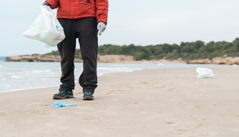 a volunteer helps pick up litter on a beach