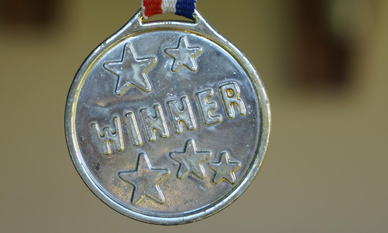 A silver-coloured medal in close up. It says 'winner' and has stars embossed on it.
