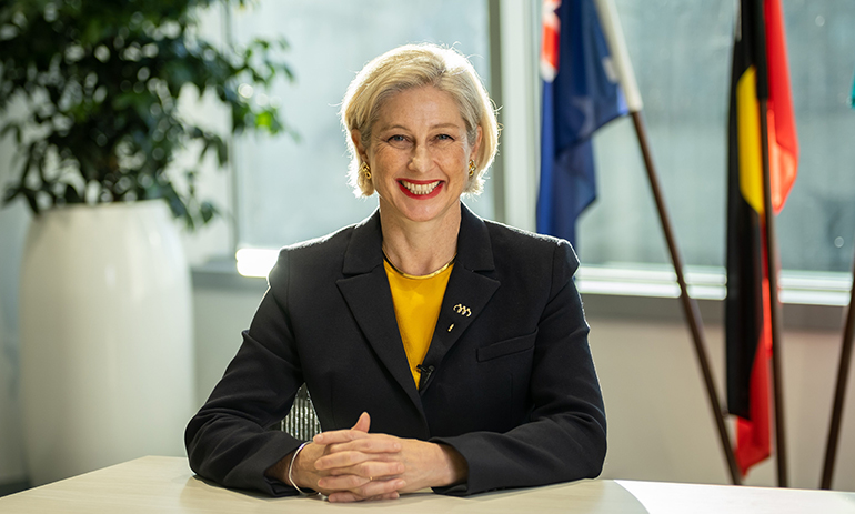 Melina Morrison sitting at her desk wearing a yellow top and black jacket