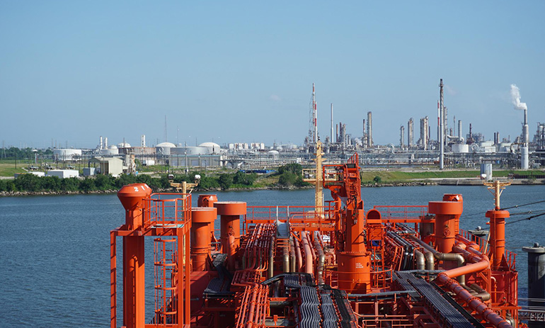 A red gas plant in the foreground with a city in the background, across the water.