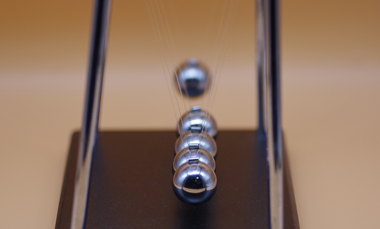 A Newton's Cradle in close-up profile: one of the silver balls is swinging back, about to hit the others.