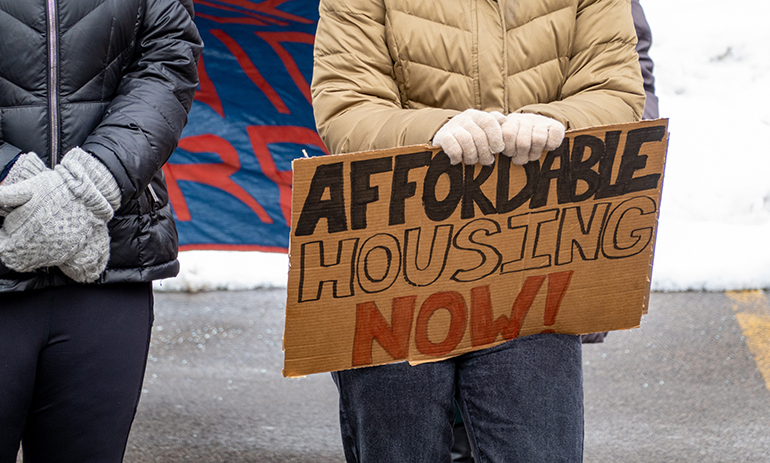 person holding a cardboard sign saying "affordable housing now"