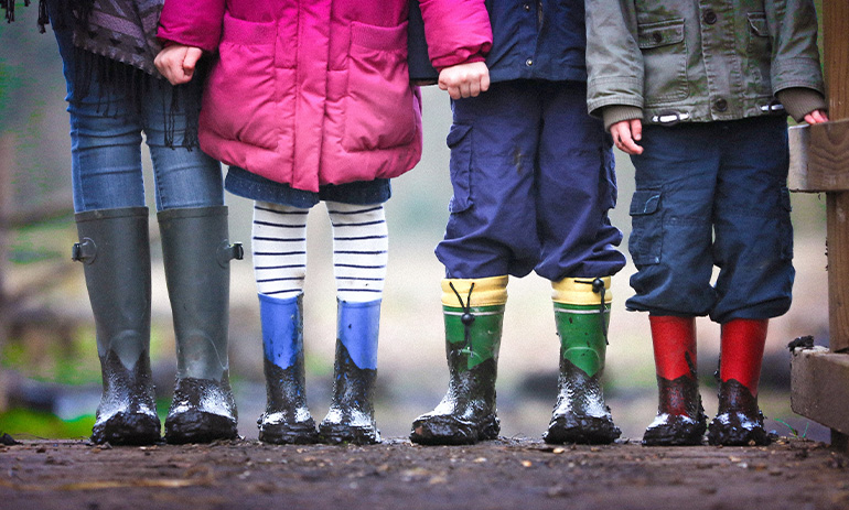 Four children stand in a row. They are wearing colourful gumboots and it looks wet and muddy.