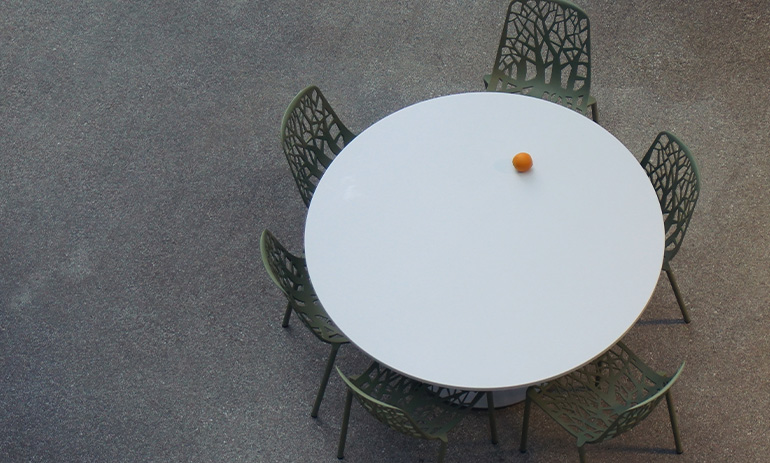 A white circular table with an orange fruit on it, surrounded by six black chairs.