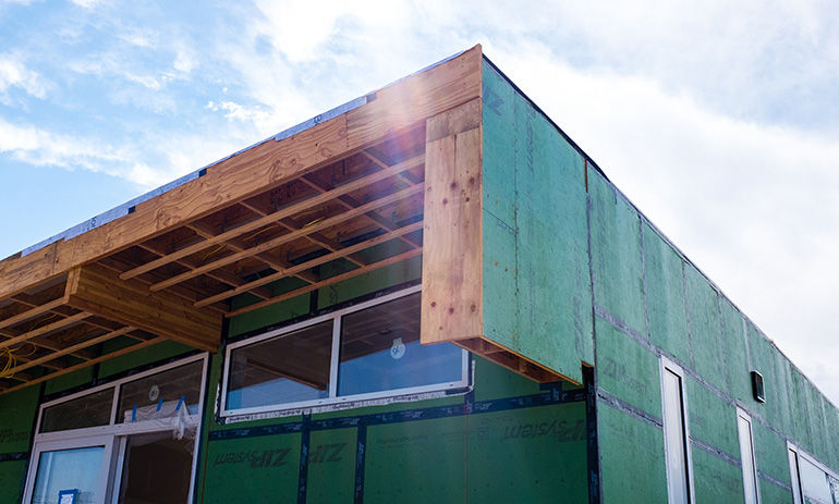 A home under construction in the sunshine, showing the insulating wrap around the frame.
