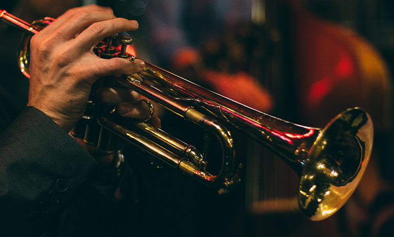 An artistic shot of a person playing a trumpet. Only their hand and the instrument is available.