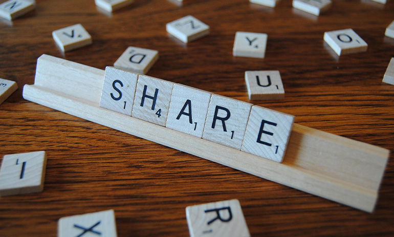 Scrabble tiles make up the word 'share' on a tile board.