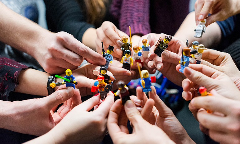 We see a the hands of a group of people, all holding different Lego figures.