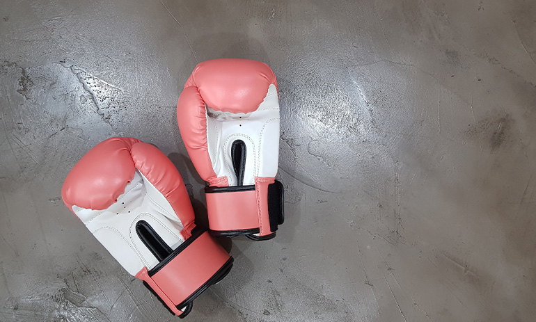 A pair of pink boxing gloves on a grey concrete floor.