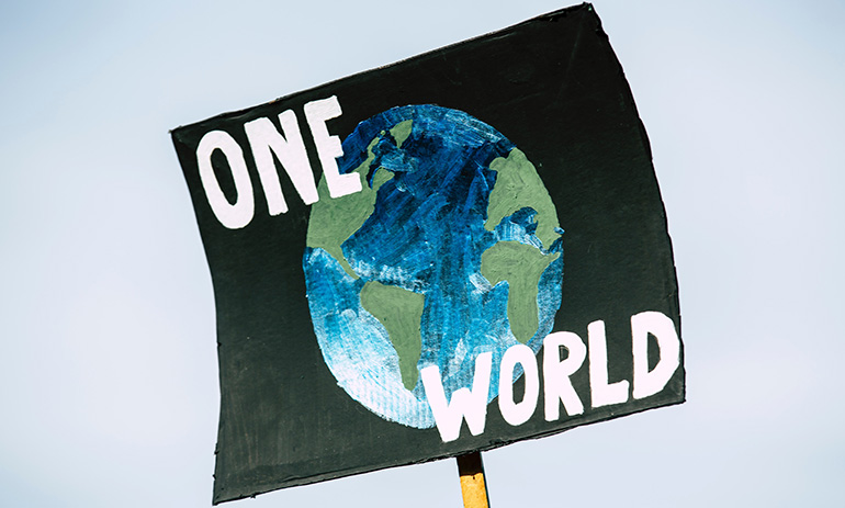 A handmade sign that says 'one world' in white letters against an image of the Earth on a black background. It looks like a sign a person would take to a protest march.