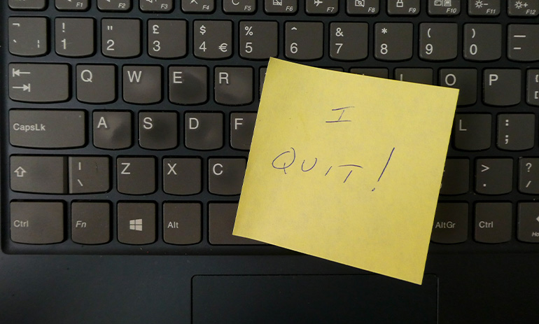 A black computer keyboard with a yellow post it note stuck to it saying I Quit