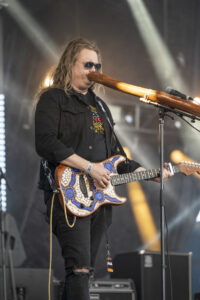 Scott Darlow stands on stage behind a microphone, playing his guitar.