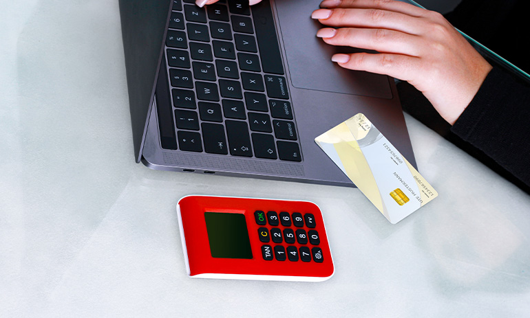 A woman types on a laptop. We can only see her hand. Next to her is a calculator and credit card.