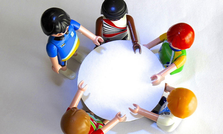 Five toy figures sit at a round table. We see them from above.