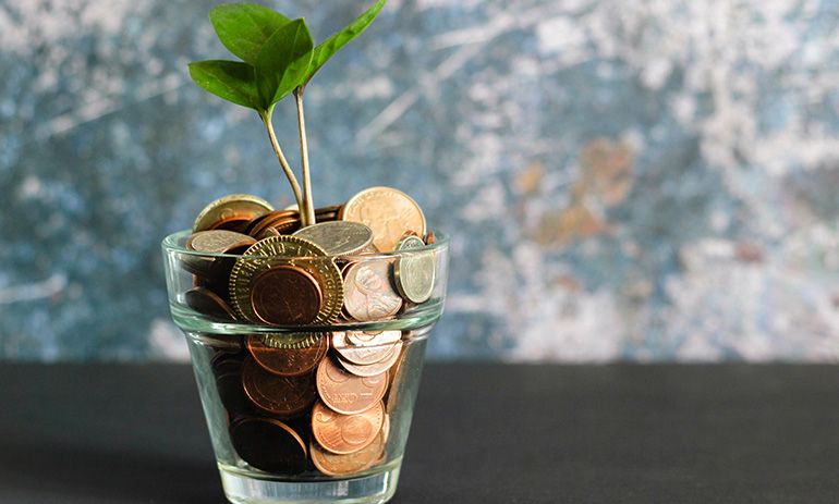A glass planter pot, filled with coins, with a small plant growing out the top.