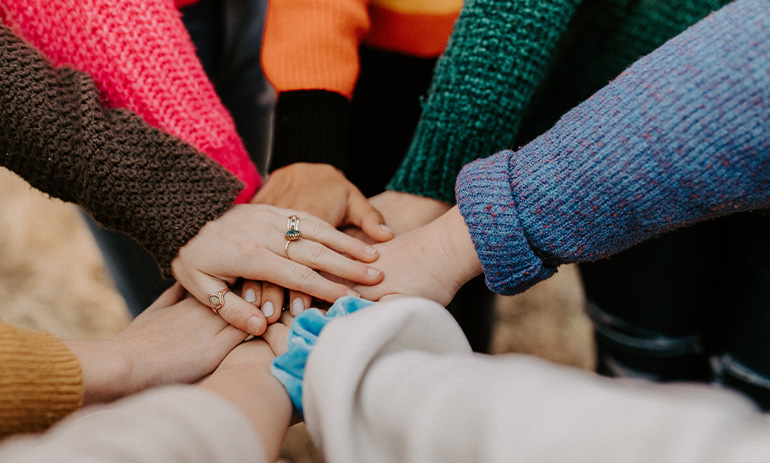 a group of people with their hands together in a circle, in a gesture of support