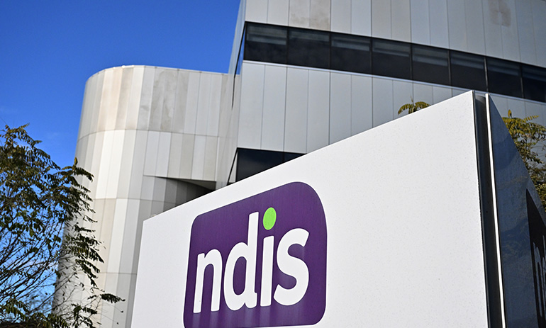 A grey building with the purple NDIS logo on it. The logo is the letters NDIS in white on a purple background