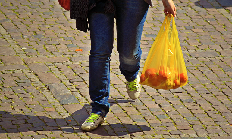 We see a person's legs, mid step. They are carrying an orange plastic bag filled with fruit.