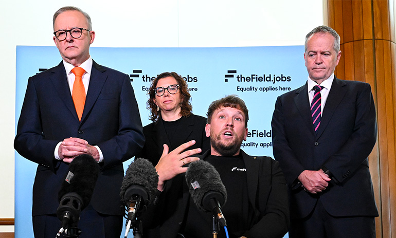 Four people stand in front of a banner with the logo for The Field: from left, Prime Minister Anthony Albanese, social services minister Amanda Rishworth, Australian of the Year Dylan Alcott who uses a wheelchair, and NDIS minister Bill Shorten. Dylan is speaking into a microphone.