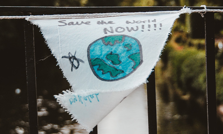 A bridge railing with a cloth poster tied to it that says save the world now, with a handdrawn picture of the earth.