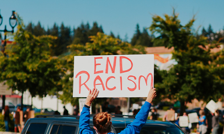 A person holds a sign at a rally that says End Racism in red letters.