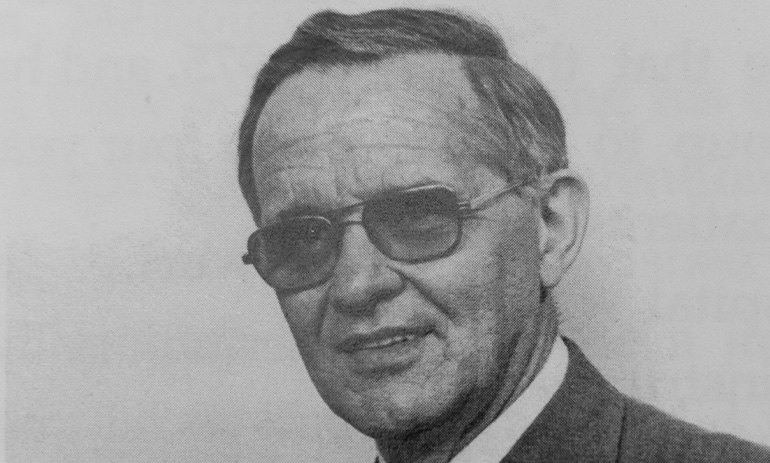 A grey, old photo of an elderly man wearing glasses and a suit. We only see his face and some of his shoulder.