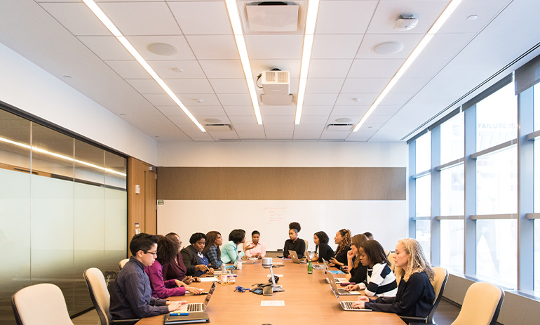 A board room table filled with employees in a light filled room.