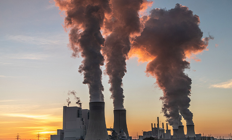 A power plant at sunset, with huge clouds of steam and smoke coming out of the chimneys.