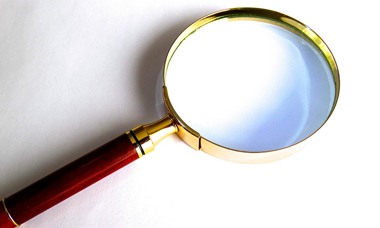 A magnifying glass on a white background. The glass has a gold metal band around the glass and a wooden handle.