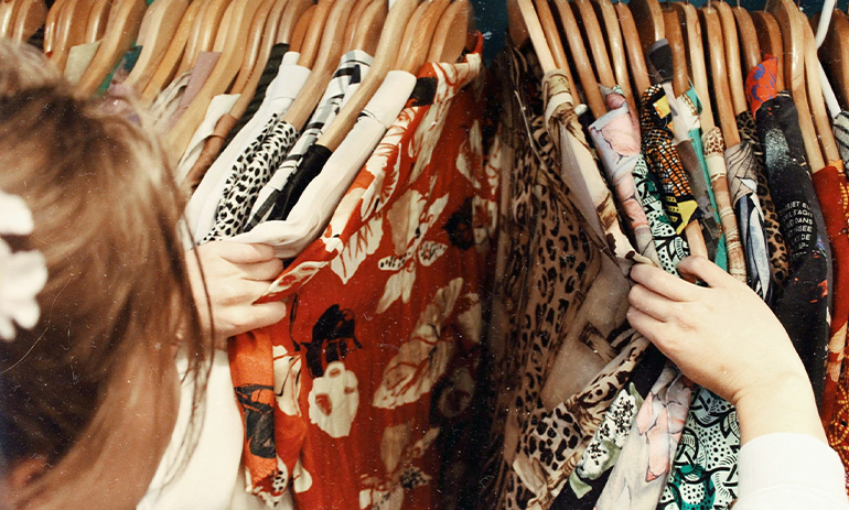 A person looks through a rack hung with many items of clothing.