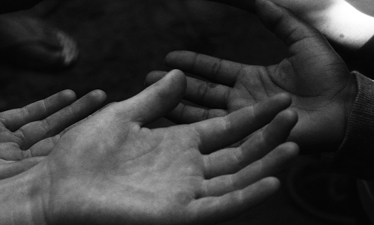 A black and grey image of hands outstretched, in a gesture of volunteering and helping. We can only see the hands.