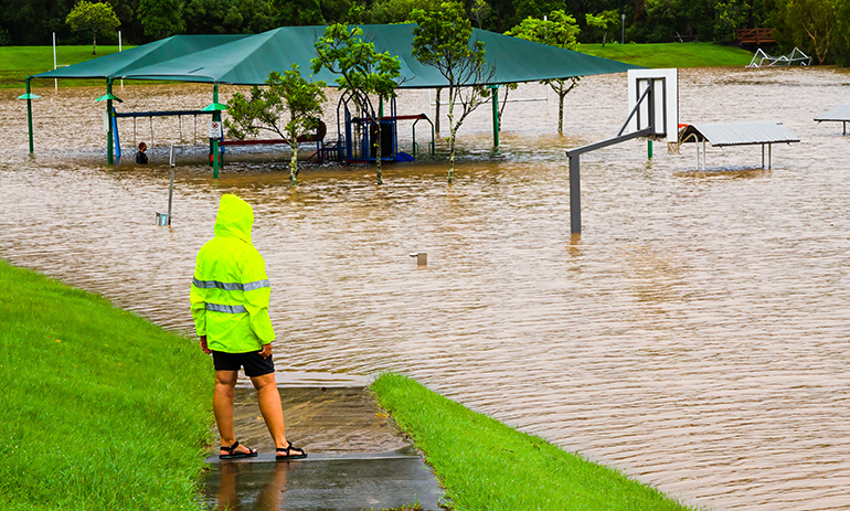 Person in a high-vis jacket looking at a flooded playground.