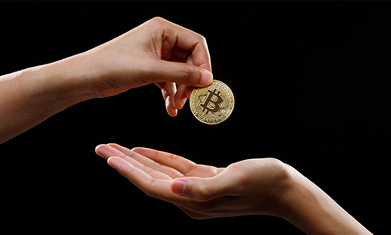 One hand passing a bitcoin to another hand.