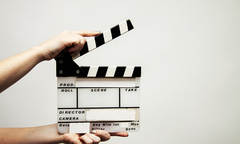 A black and white clapperboard, used in the screen industry. It is being held by a person who is able to clap it.