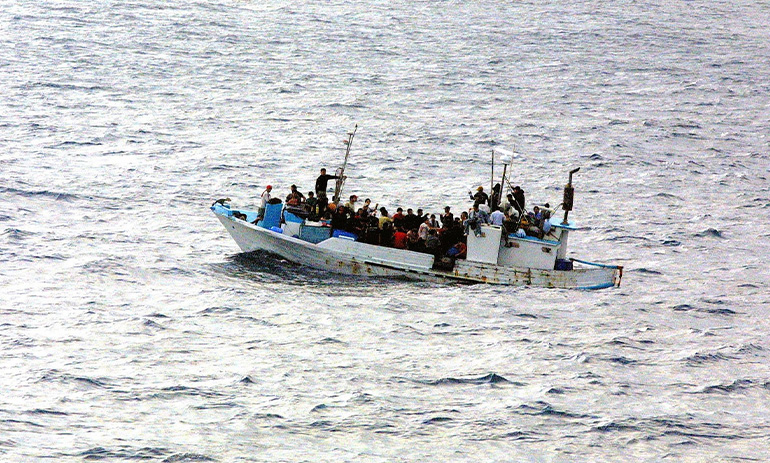 A boat filled with people, crossing open water. The implication is the boat is a boat filled with asylum seekers and refugees.